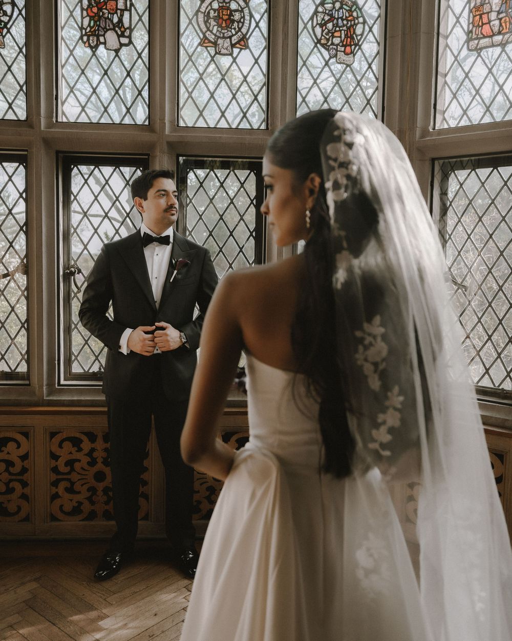 Bride and groom share intimate moment by ornate stained glass windows indoors.