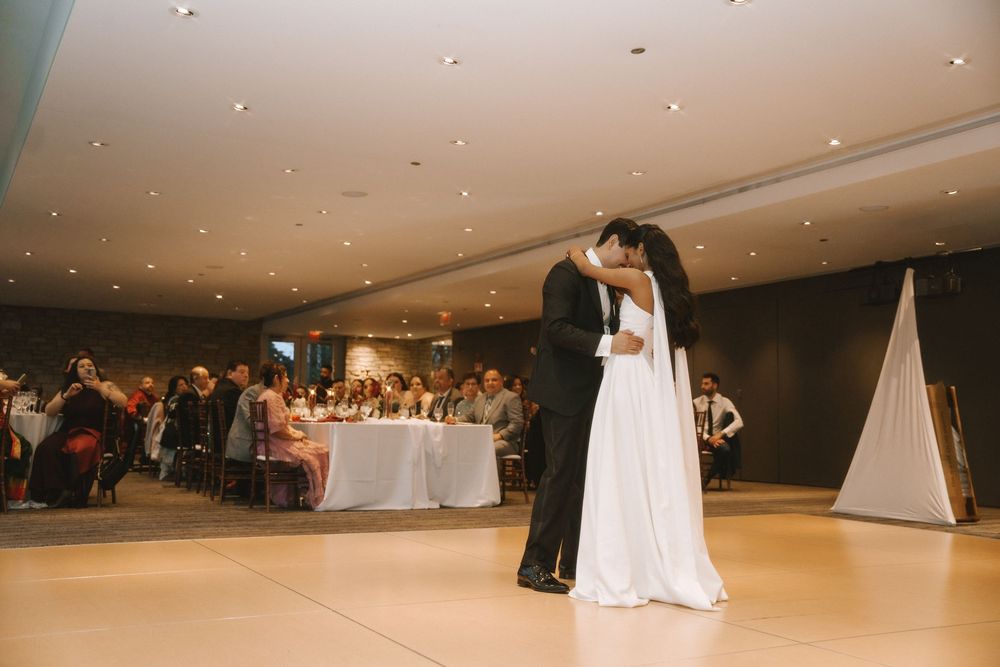 Bride and groom share their first dance at wedding reception while guests watch from decorated tables in elegant venue.