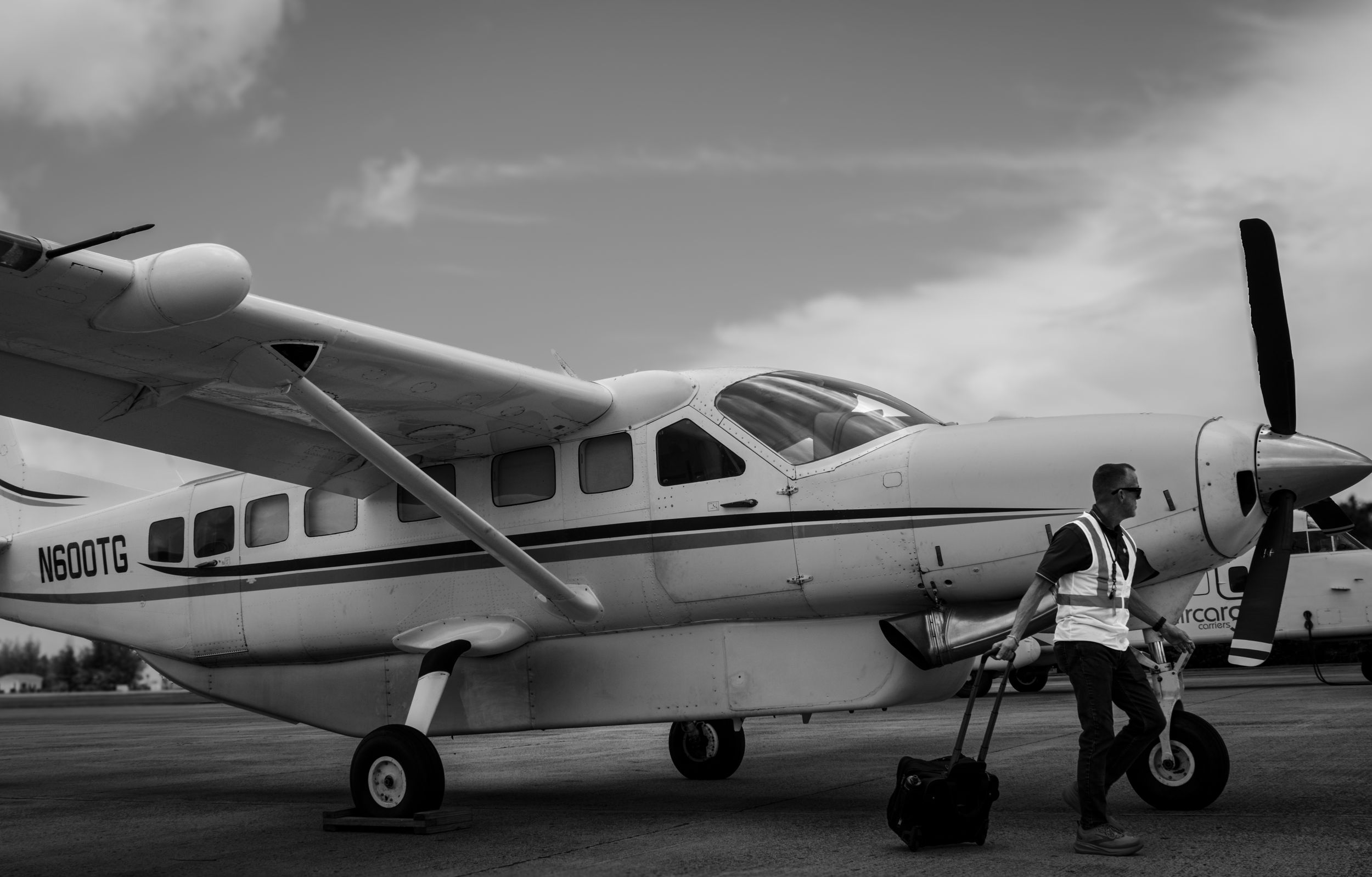 Black and white photo of ground crew member walking beside small propeller aircraft on tarmac.
