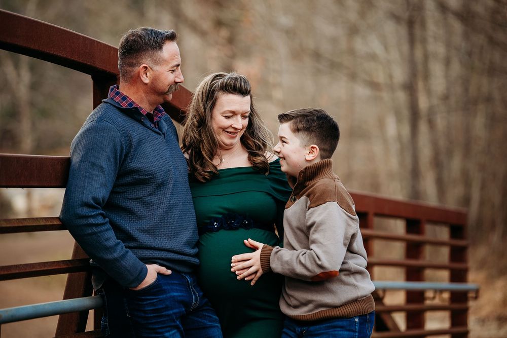 Expectant parents and young son sharing a joyful moment on a bridge during maternity photos.