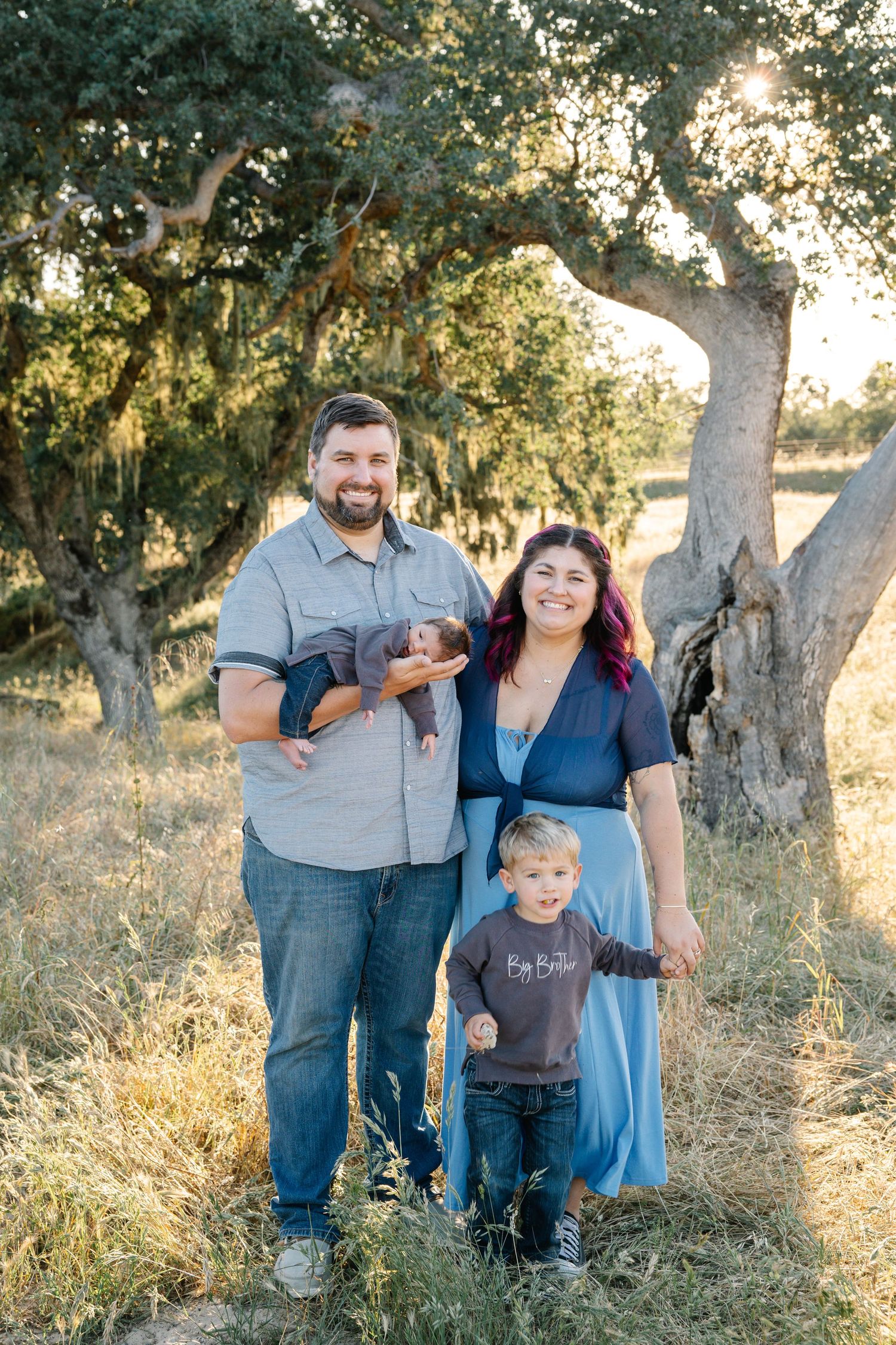 family of four with new baby and big brother, standing in the oak trees