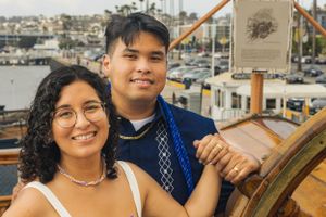 A couple poses for photos with a marina and boats in the background. Shot By Zeus Holbrook San Diego Wedding Photographer