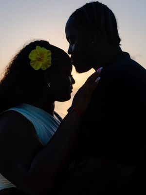 Romantic silhouette of a couple about to kiss at sunset, woman wearing yellow flower in hair.
