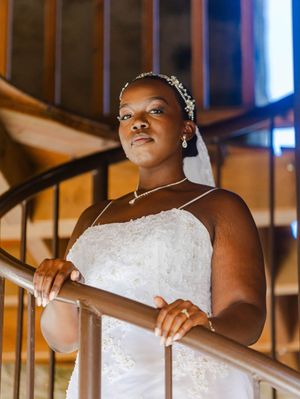 Elegant bride in white strapless gown with floral headpiece poses gracefully on wooden staircase railing.