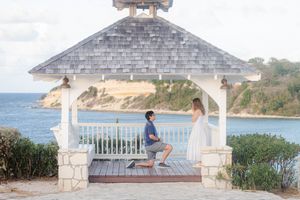 Man proposing to woman in a white gazebo overlooking a tropical ocean coastline on a sunny day.