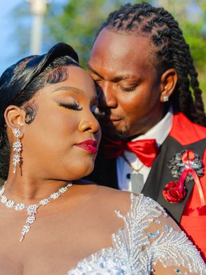 Elegant Black couple in wedding attire, bride in beaded gown with diamond jewelry, groom in red tuxedo with bow tie.