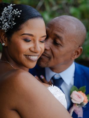 A groom in a blue suit kisses his bride wearing a white dress and floral hair accessory on their wedding day.