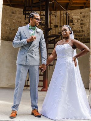 Wedding couple posing by spiral staircase, groom in light gray suit, bride in white lace A-line gown.