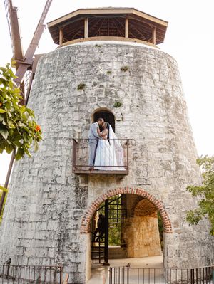 A wedding couple shares a romantic kiss on the balcony of a historic stone windmill tower.