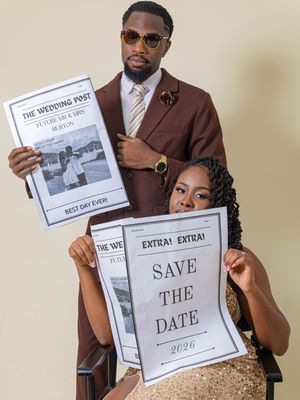 Couple poses with newspaper-themed Save the Date signs for 2026 wedding announcement photo shoot.