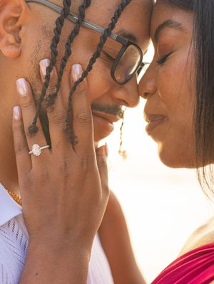 Couple sharing romantic moment with engagement ring visible on woman's hand at beach.
