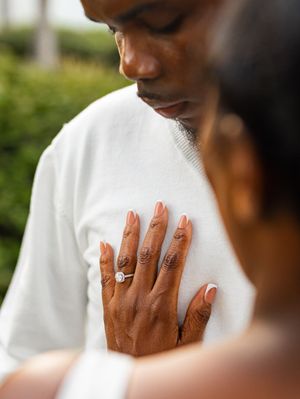 Close-up of a woman's hand with an engagement ring resting on a man's chest during a romantic outdoor moment.