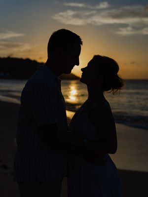 Romantic silhouette of a couple embracing on a beach at sunset with golden ocean reflections.