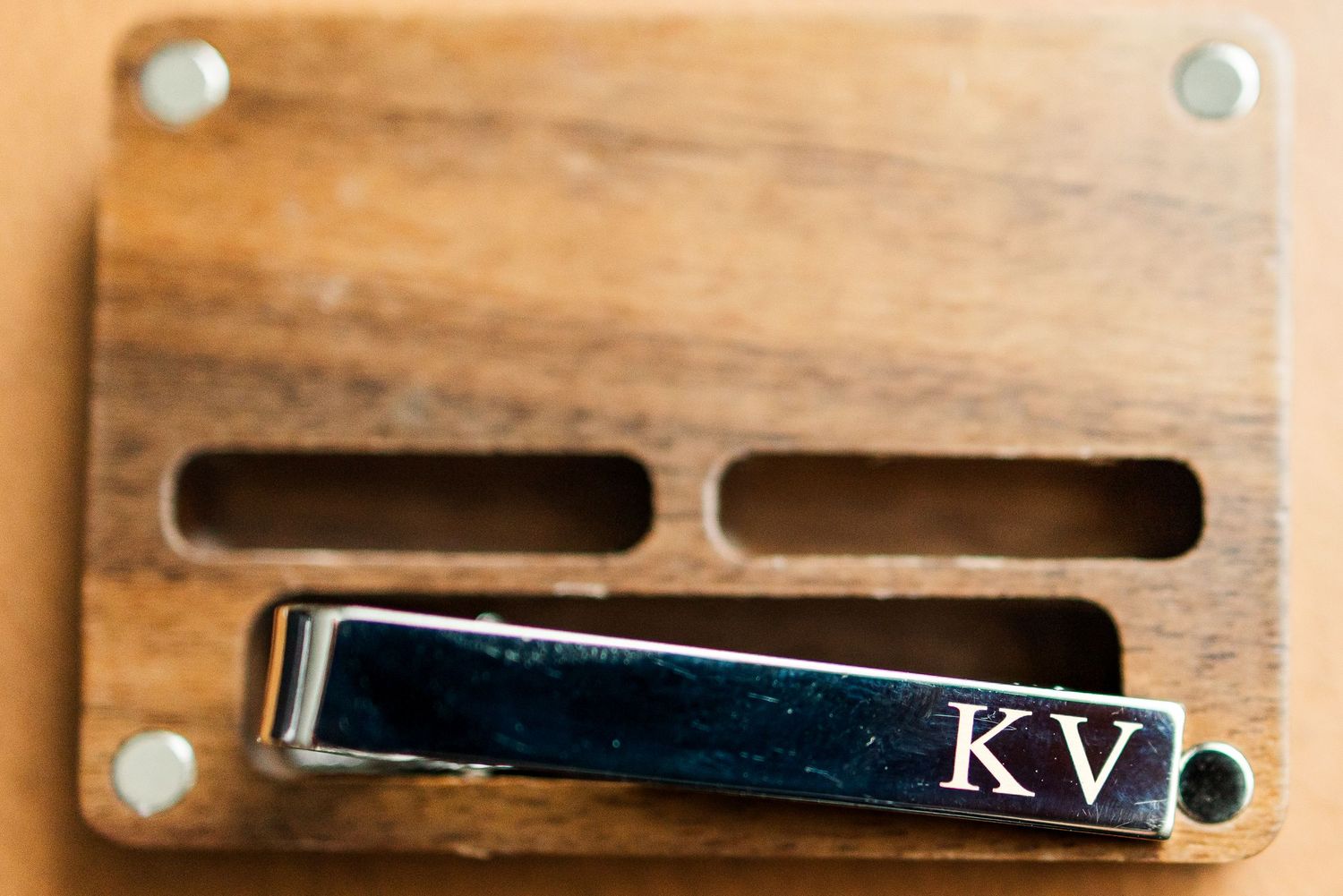 Silver tie clip engraved with initials KV resting on a wooden surface with decorative slots.