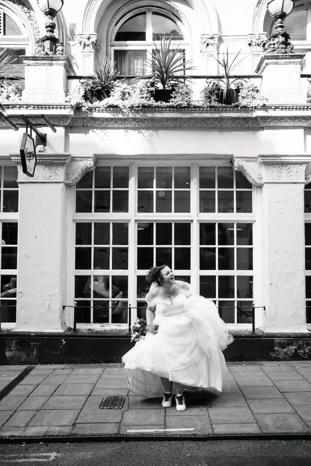 Black and white photo of a bride in a white dress and sneakers posing playfully outside after her Corn Street Registry Office Wedding