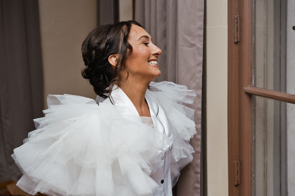 Smiling bride in white tulle ruffled wrap laughing joyfully near a doorway on her wedding day.