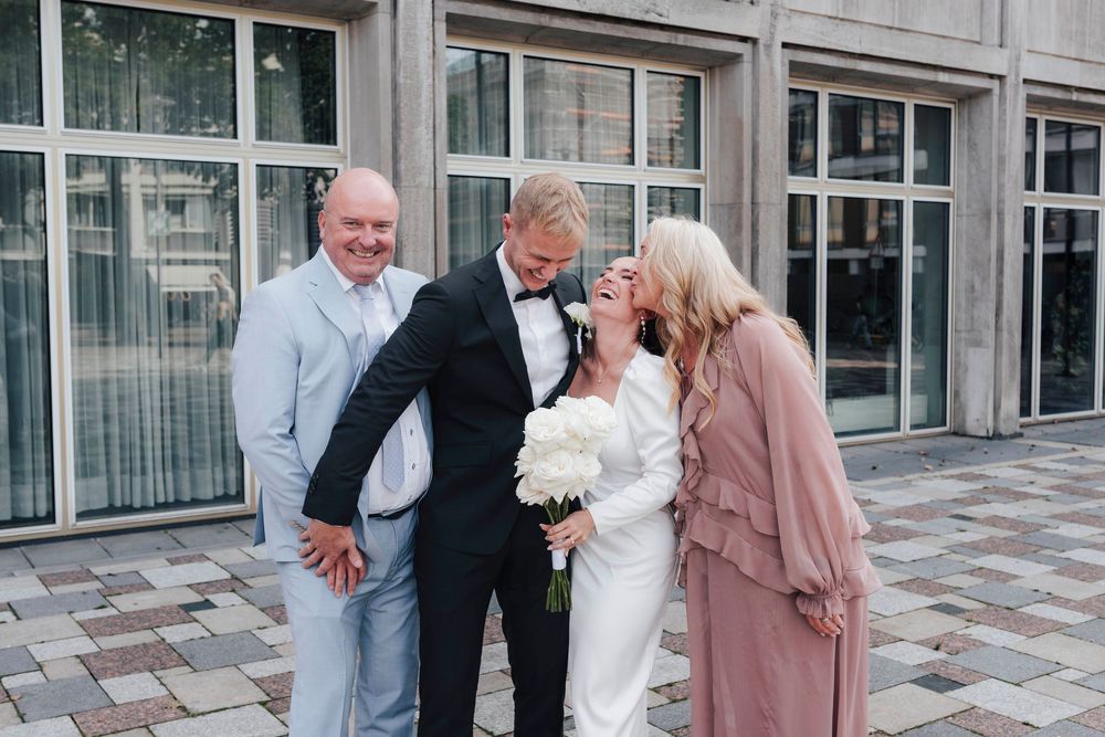 Bride and groom celebrate with parents outside a modern building on their wedding day.