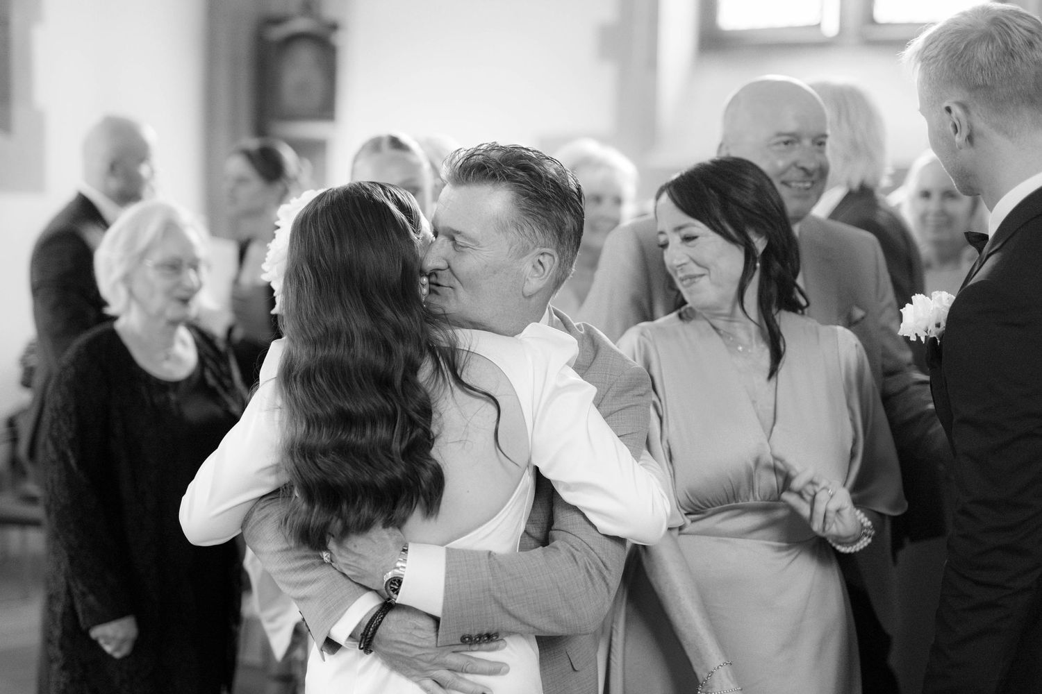 Black and white wedding photo of guests hugging and celebrating inside a church ceremony venue.