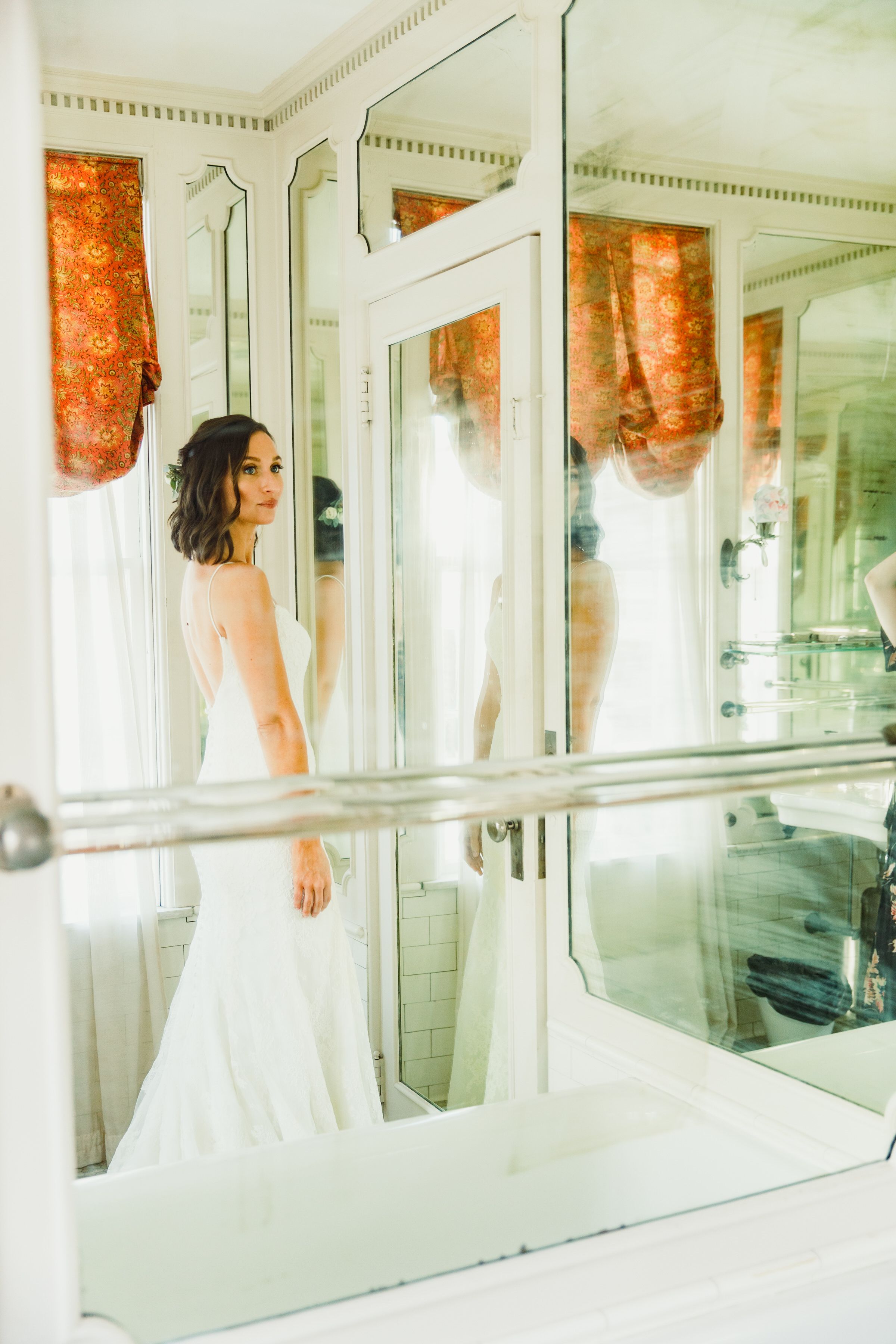 Elegant white wedding dress reflected in mirrored walls with orange curtains.