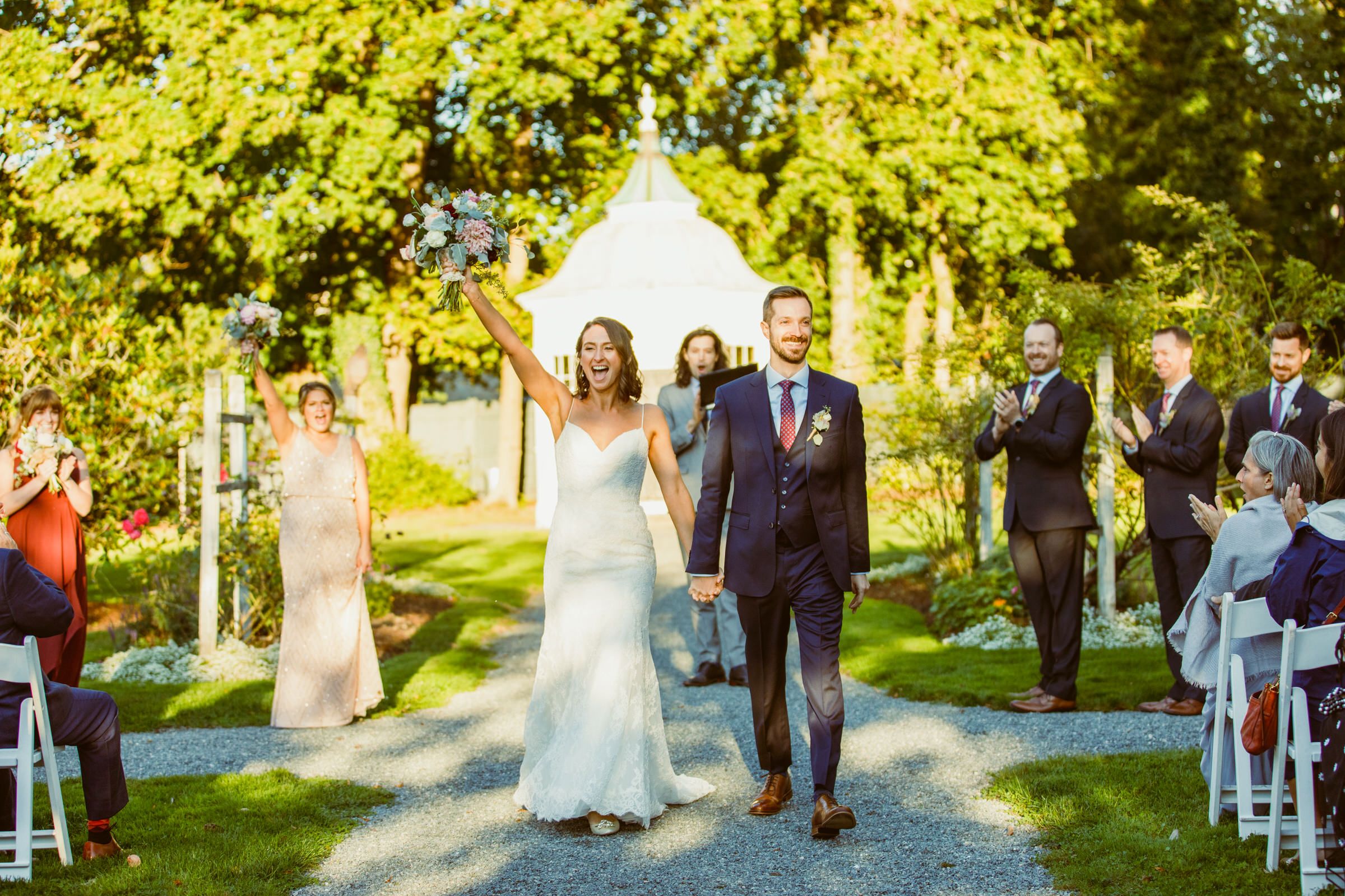 Wedding ceremony recessional on a garden path under golden sunlight.
