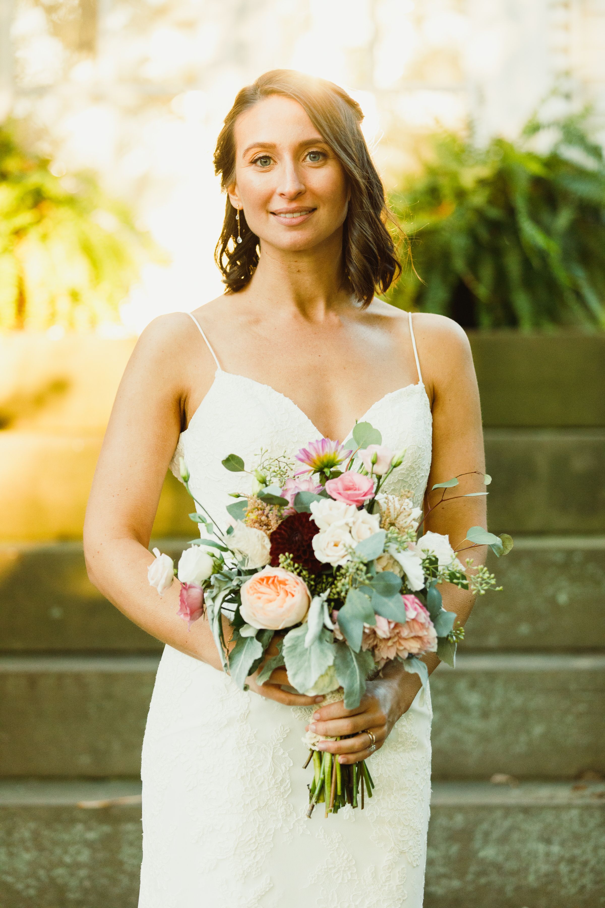A bouquet of pink and white roses with eucalyptus leaves held against a sunlit garden background.