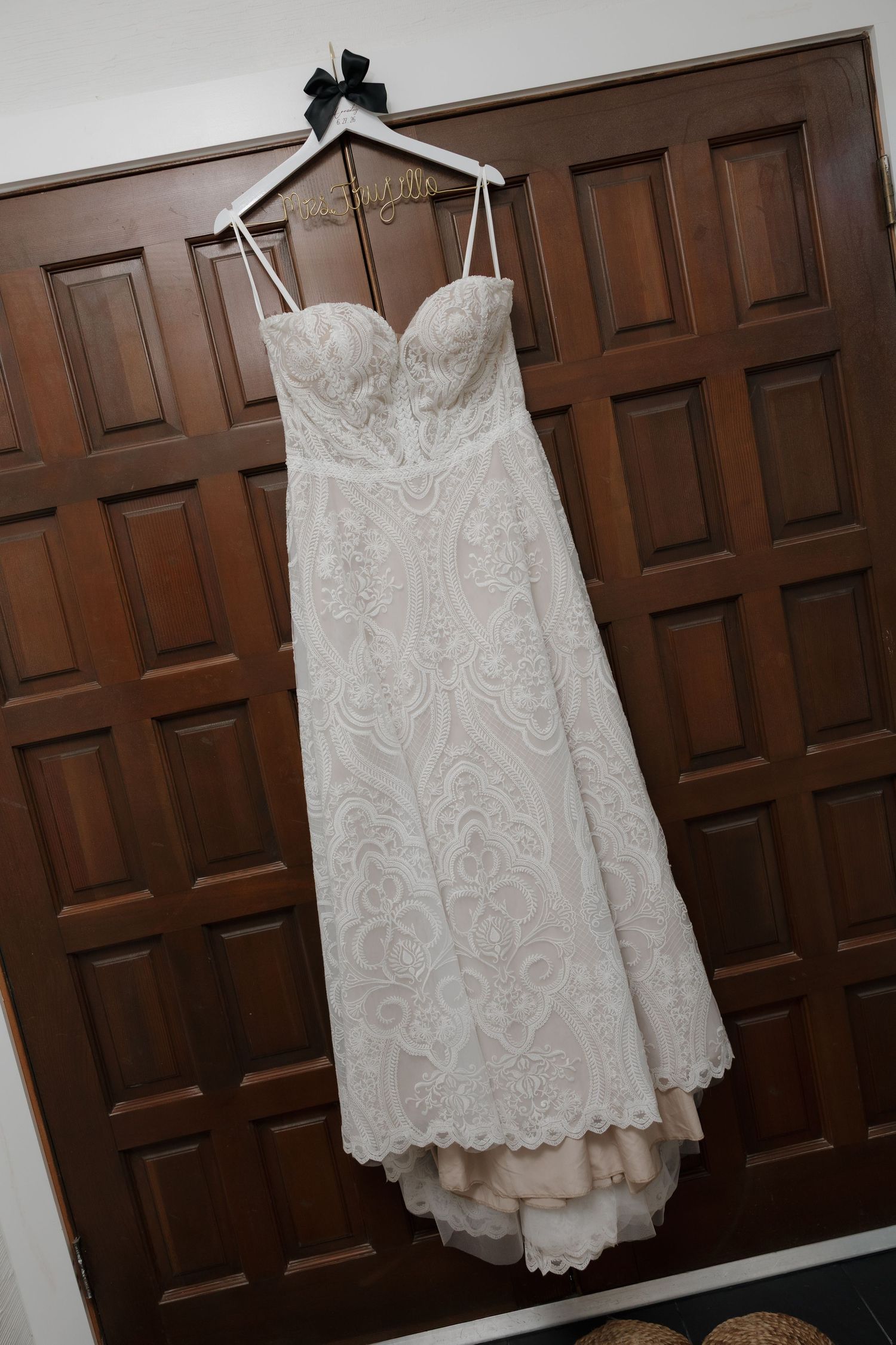 Strapless lace wedding dress with sweetheart neckline hanging on personalized hanger on wooden door.