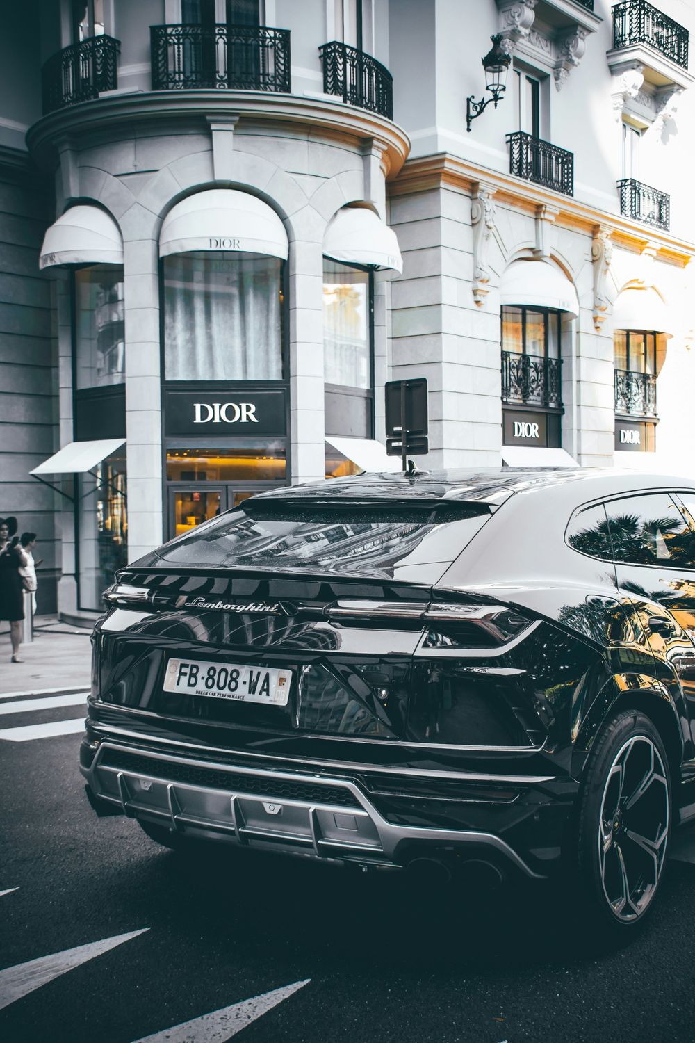 Black Lamborghini Urus SUV parked outside a Dior luxury boutique on an elegant Parisian street.