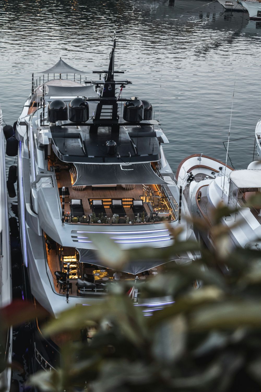 Luxury superyacht docked in a marina at dusk, featuring multiple decks with warm lighting and sleek modern design.