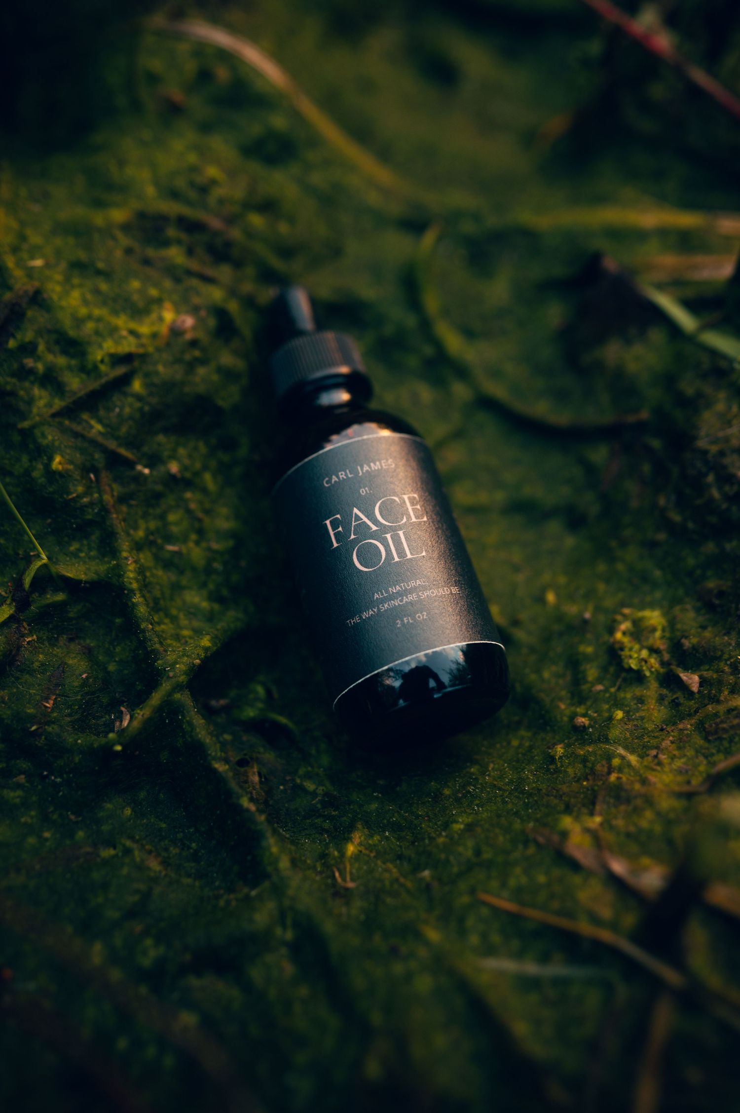 Dark glass dropper bottle of Carl James Face Oil resting on lush green moss outdoors.