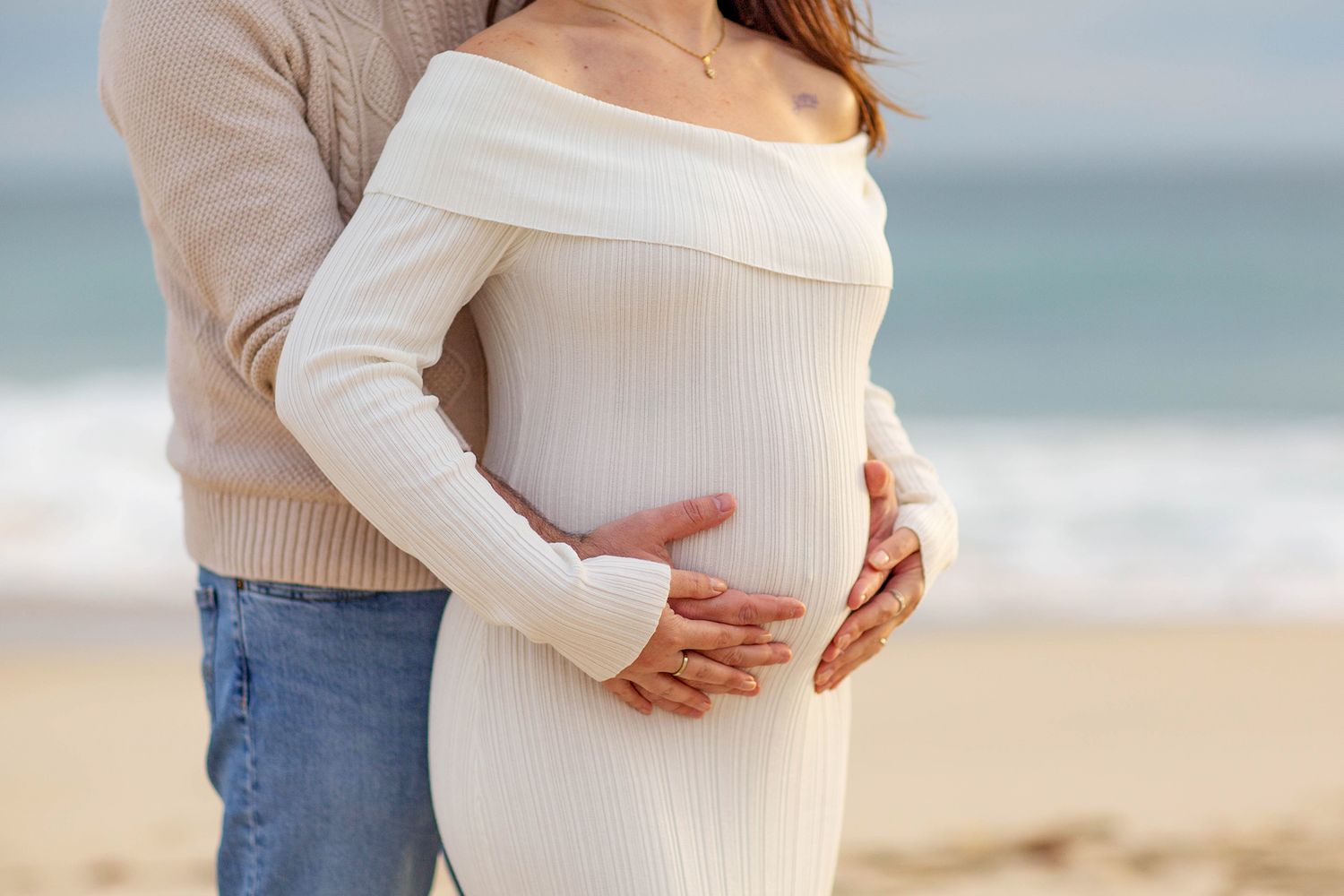 Couple embracing baby bump during golden hour on a Perth beach
