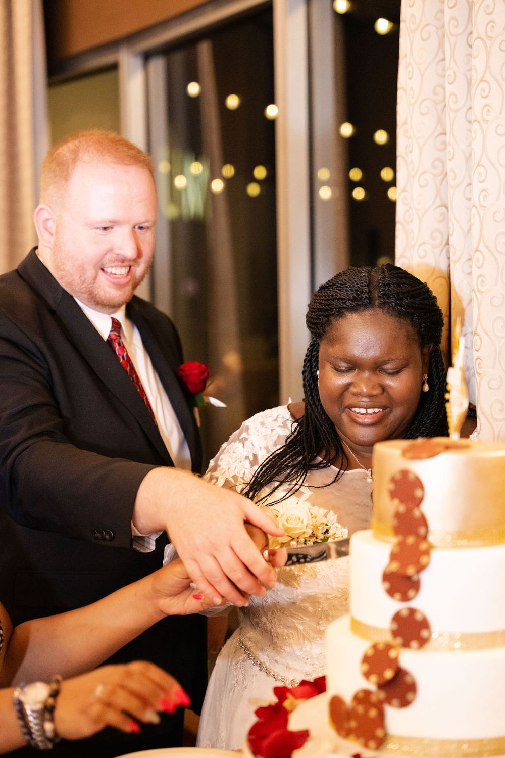 Bride and groom smiling while cutting their wedding cake together at their reception.