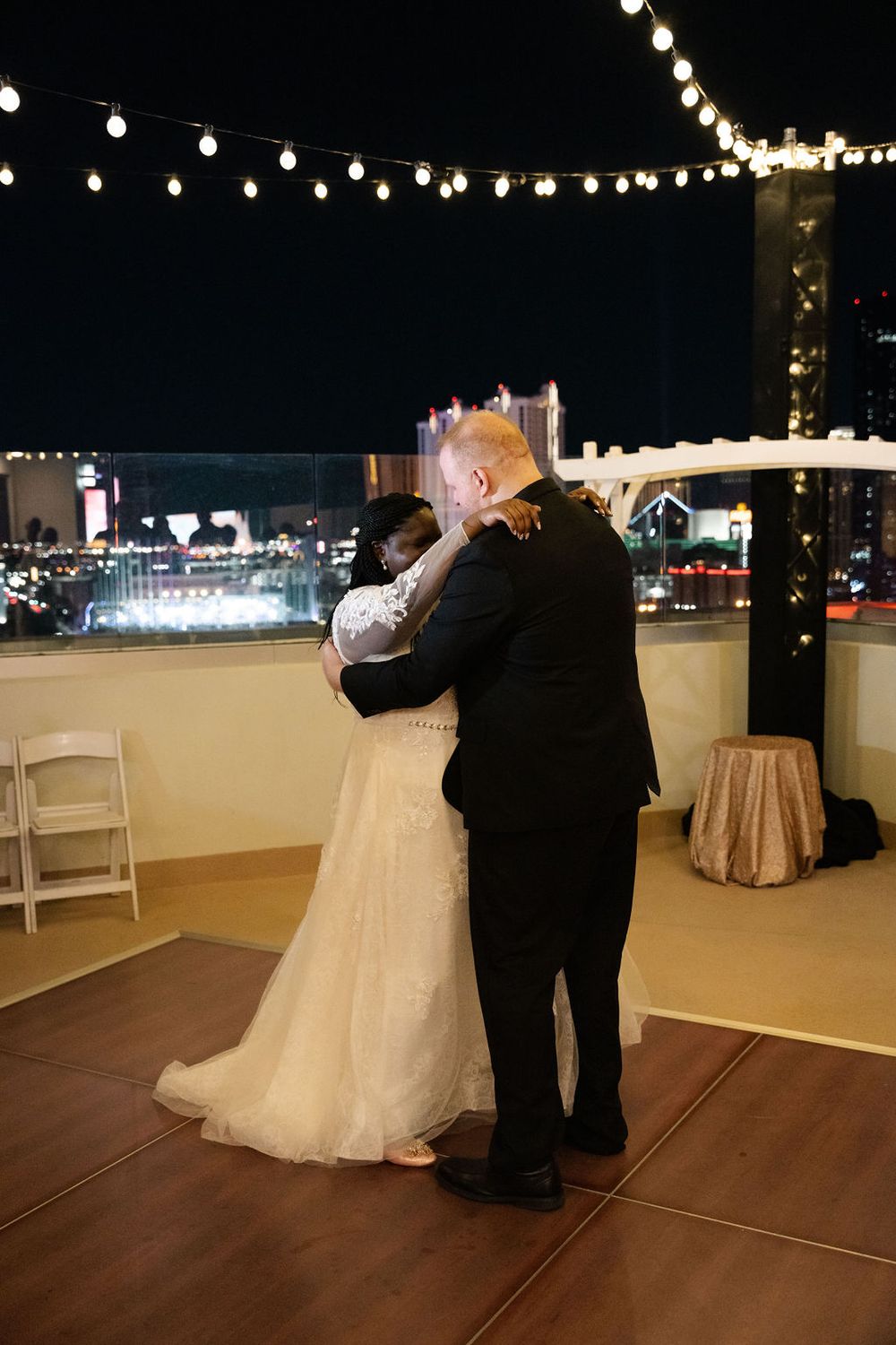 Couple shares first dance on rooftop venue at night with city lights and string lights backdrop at Las Vegas wedding.