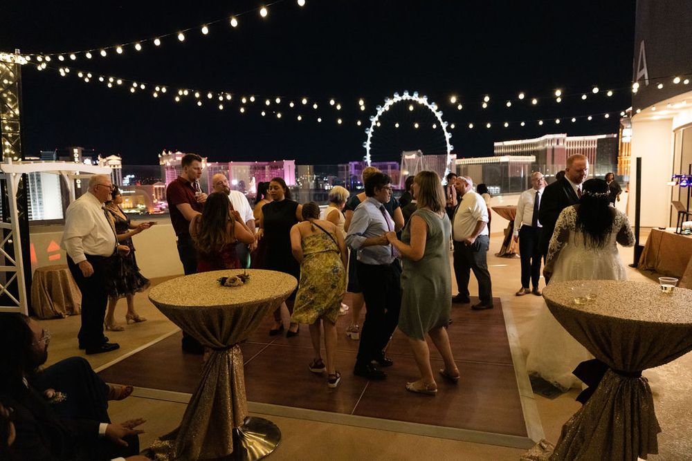 Guests mingle on a rooftop venue at night with string lights and the Las Vegas High Roller in the background.