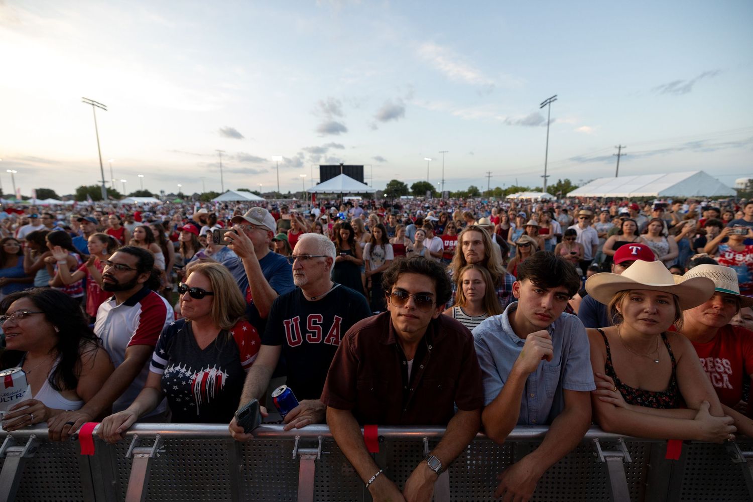 Large crowd of patriotic Americans gathered at an outdoor Fourth of July celebration event at dusk.