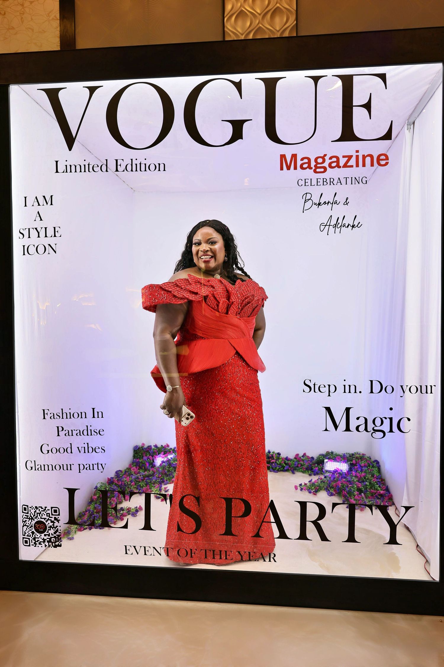 Woman in red lace dress posing inside a Vogue Magazine Limited Edition Let's Party photo booth.