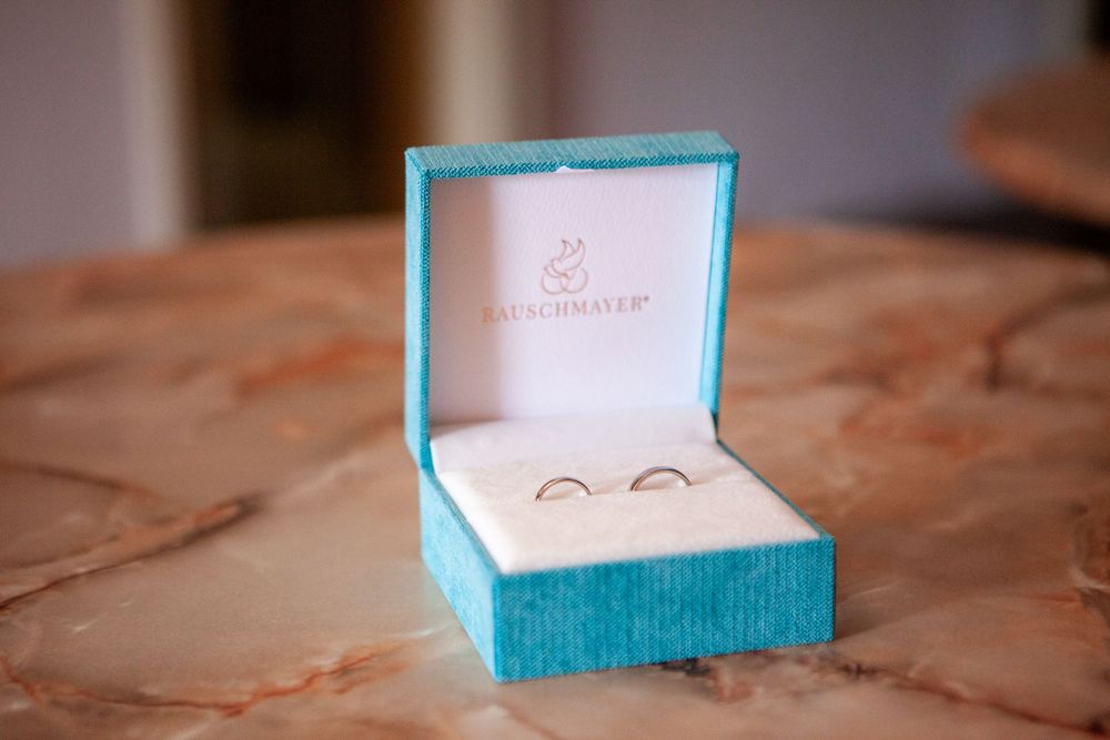Two gold wedding bands displayed in an open turquoise Kauschinger jewelry box on a marble surface.
