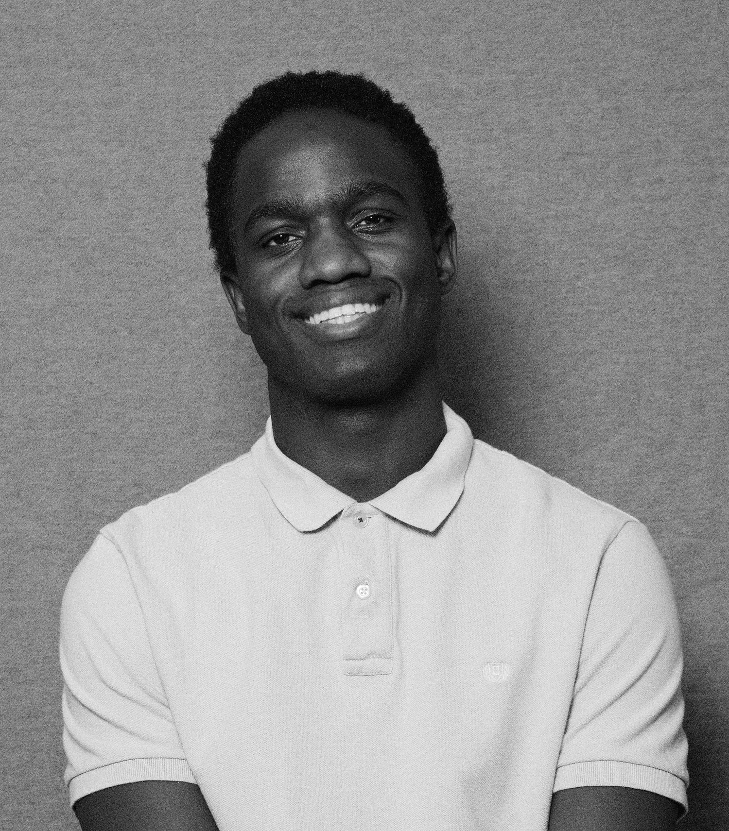 Smiling young man in a white polo shirt poses against a gray background in a black and white portrait photo.