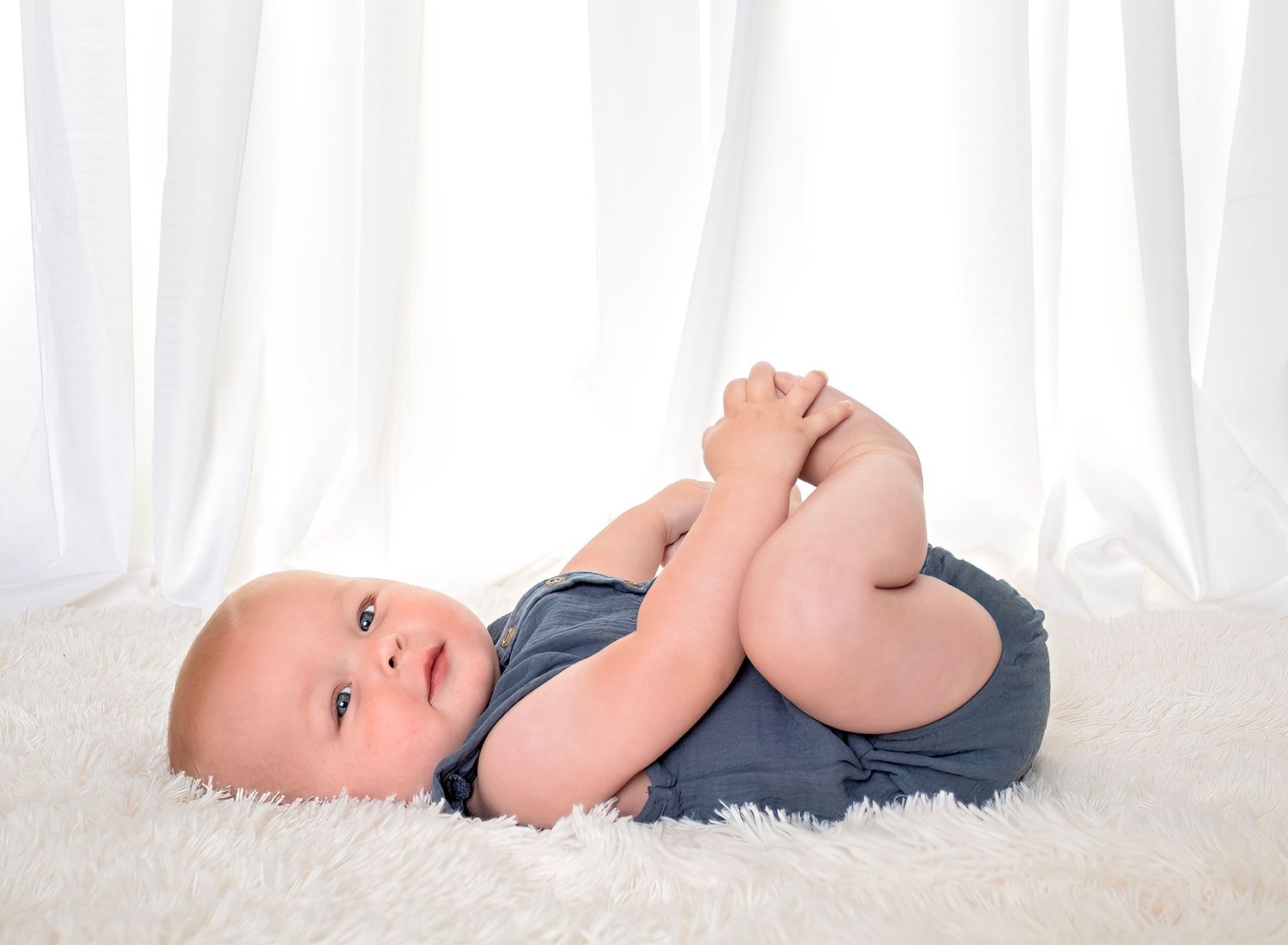 A peaceful newborn baby sleeping curled up on a soft knit blanket, with tiny hands tucked under their chin.