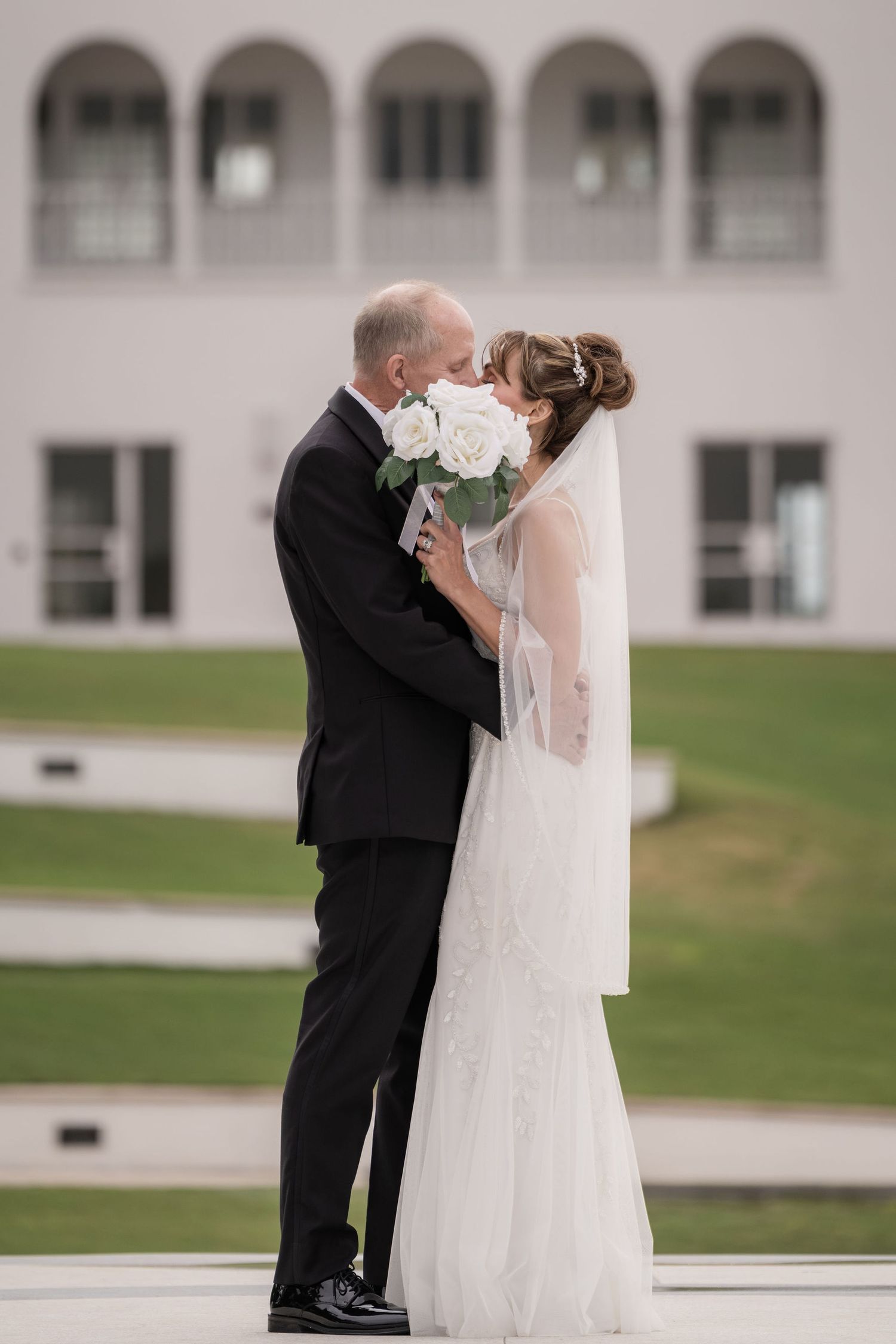 Couple sharing a kiss behind the bride's bouquet with the Mansion at Tuckahoe arches behind them