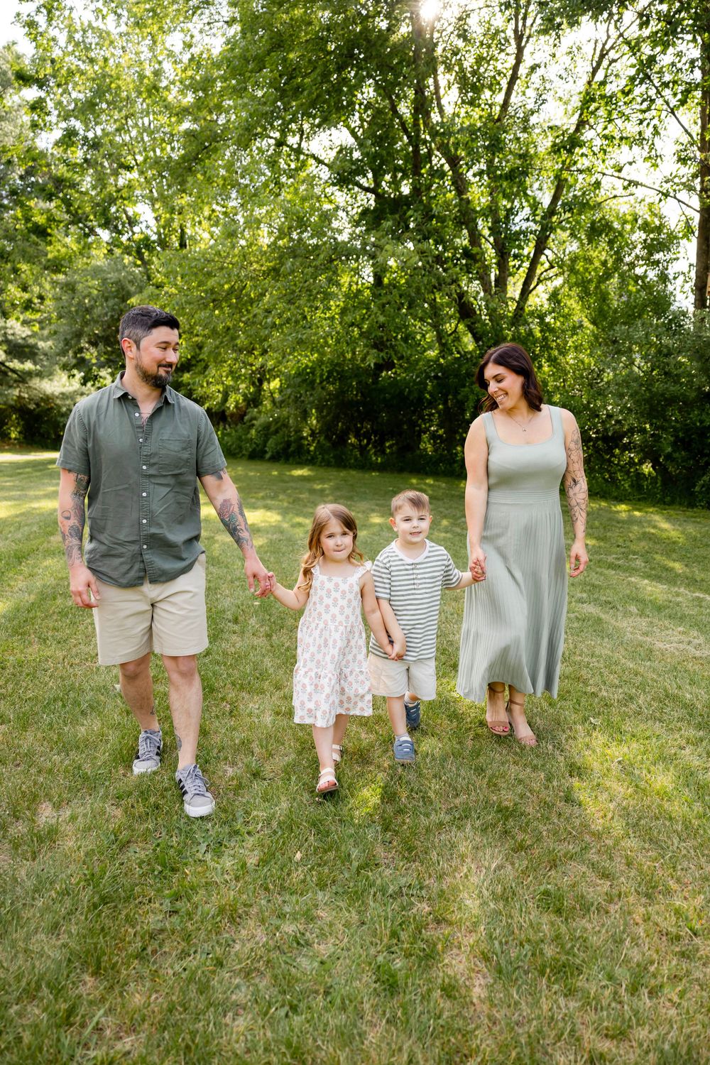 Family of four walking hand-in-hand through a lush green park on a sunny day.