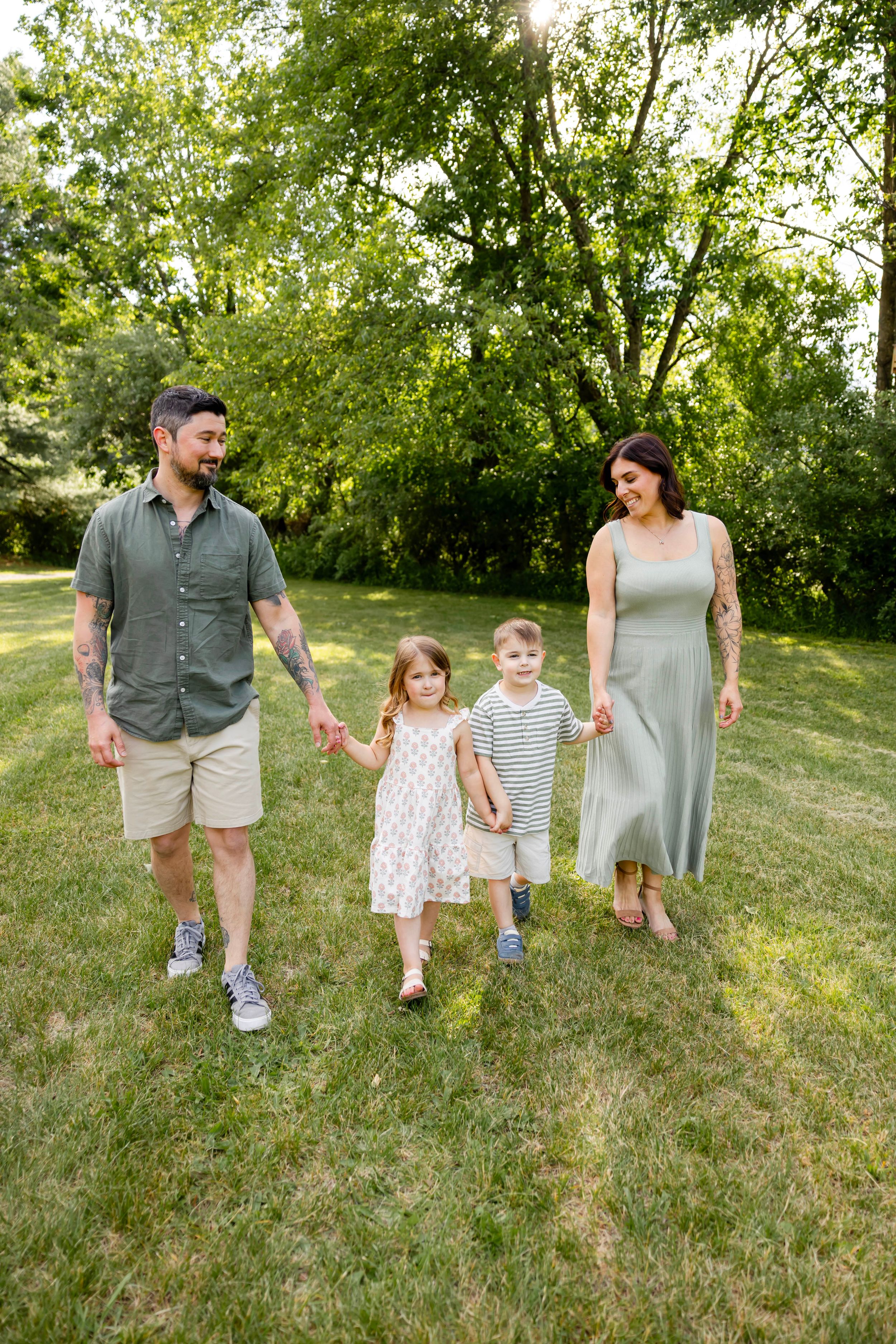 Family of four walking hand-in-hand through a lush green park on a sunny day.