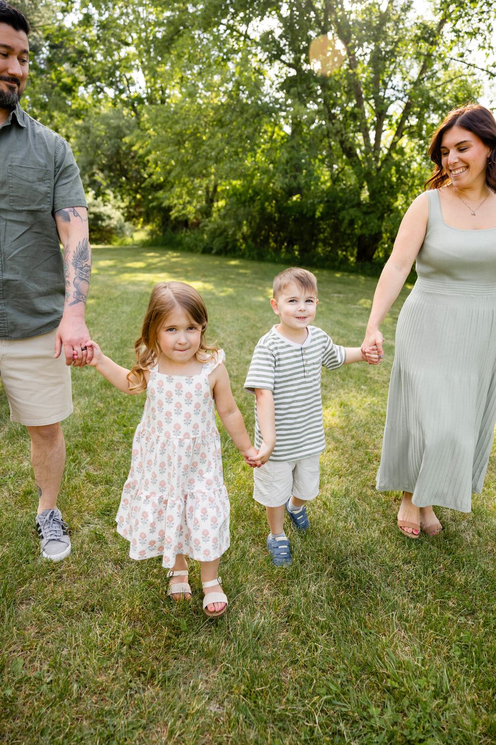Happy family of four holding hands and walking together on green grass in a sunny backyard park setting.