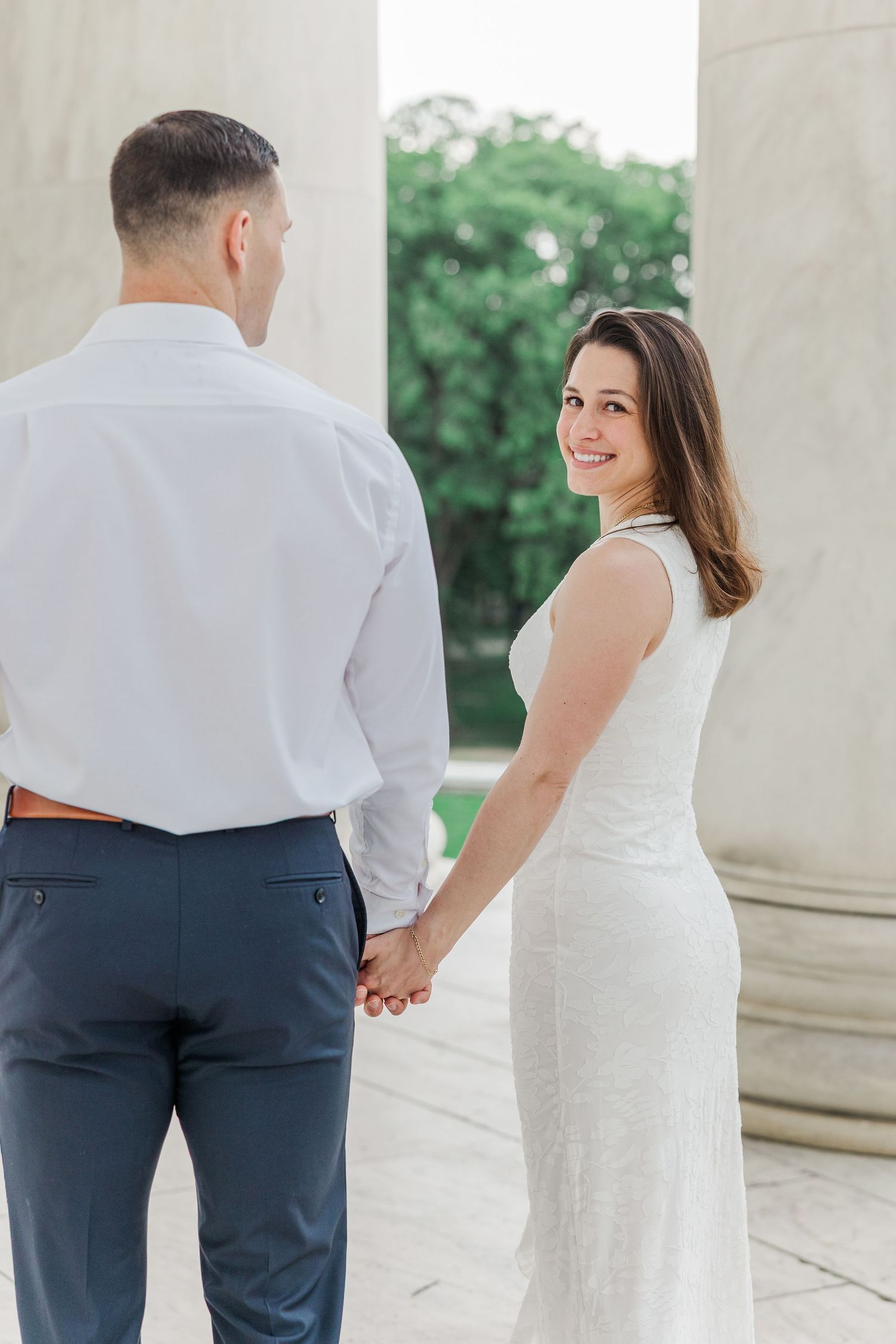 A bride in a white dress holds hands with a groom in a white shirt at the Jefferson Memorial.