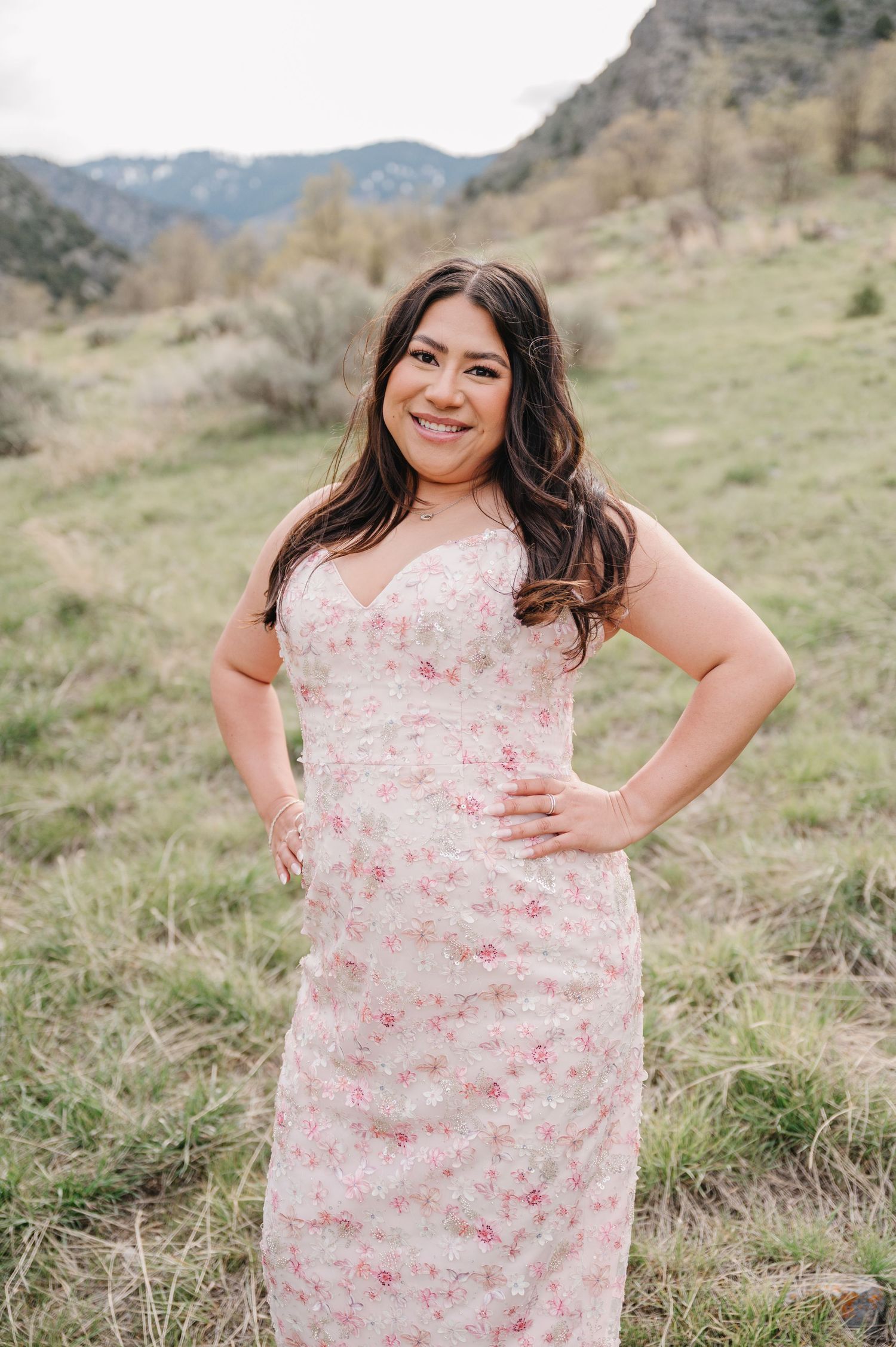 A floral pink dress set against a backdrop of rugged mountains and natural grassland terrain.