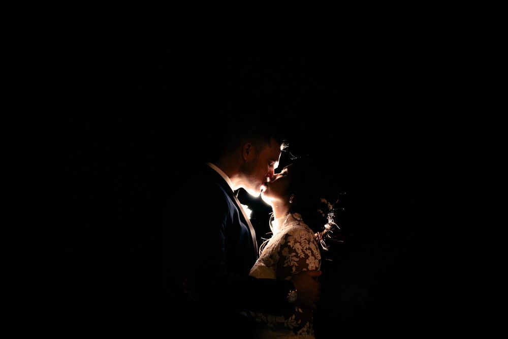 A romantic silhouette of a bride and groom sharing an intimate moment, beautifully lit against a dark background.