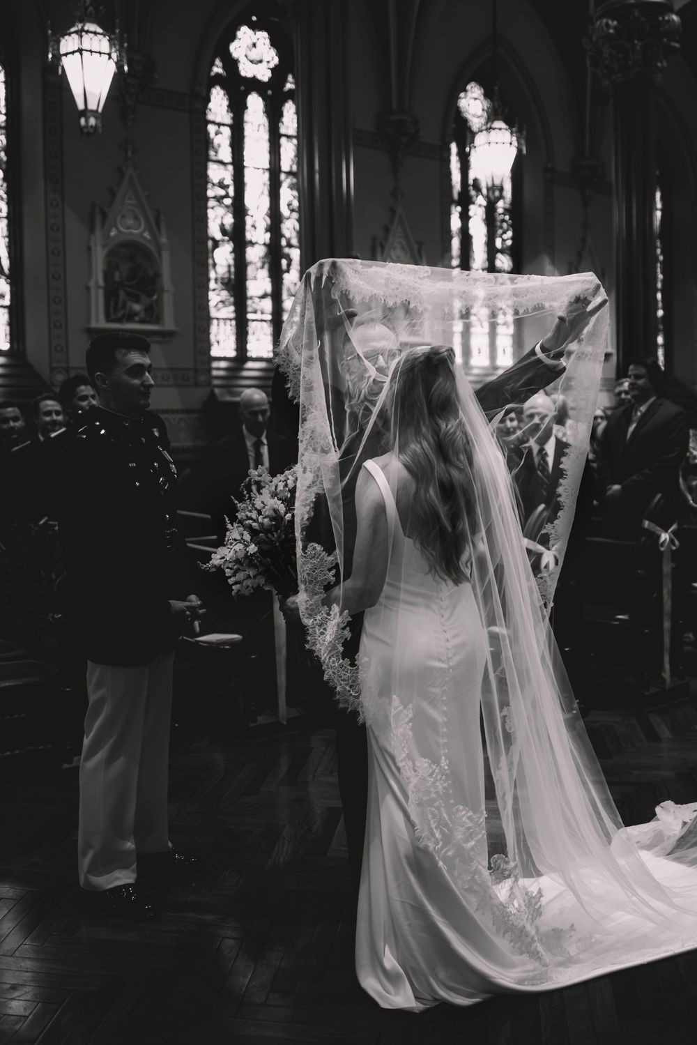 Black and white photo of a bride walking down the church aisle in a flowing gown and long veil.