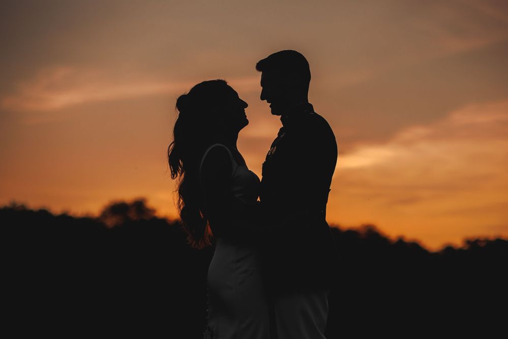 Silhouette of a romantic couple embracing at sunset with warm orange sky backdrop.