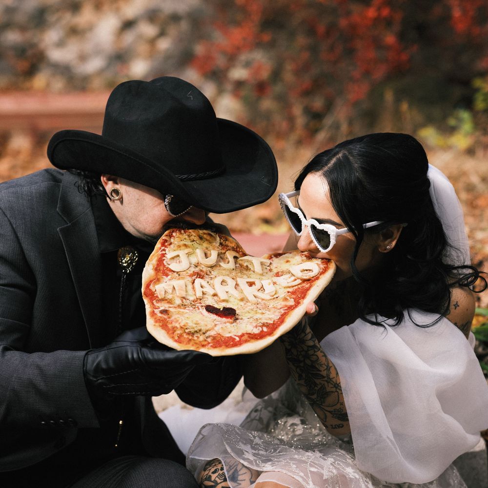 Newlyweds share a bite of pizza with Just Married written in cheese at their unique wedding celebration.