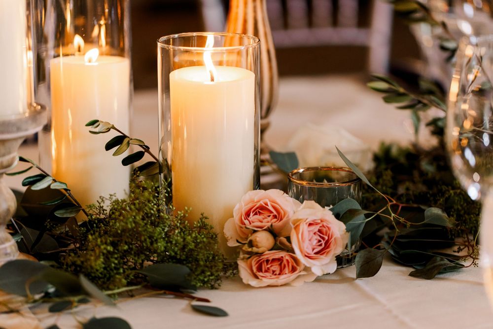 Elegant wedding table centerpiece with white pillar candles, pink roses, greenery, and moss in warm candlelight.