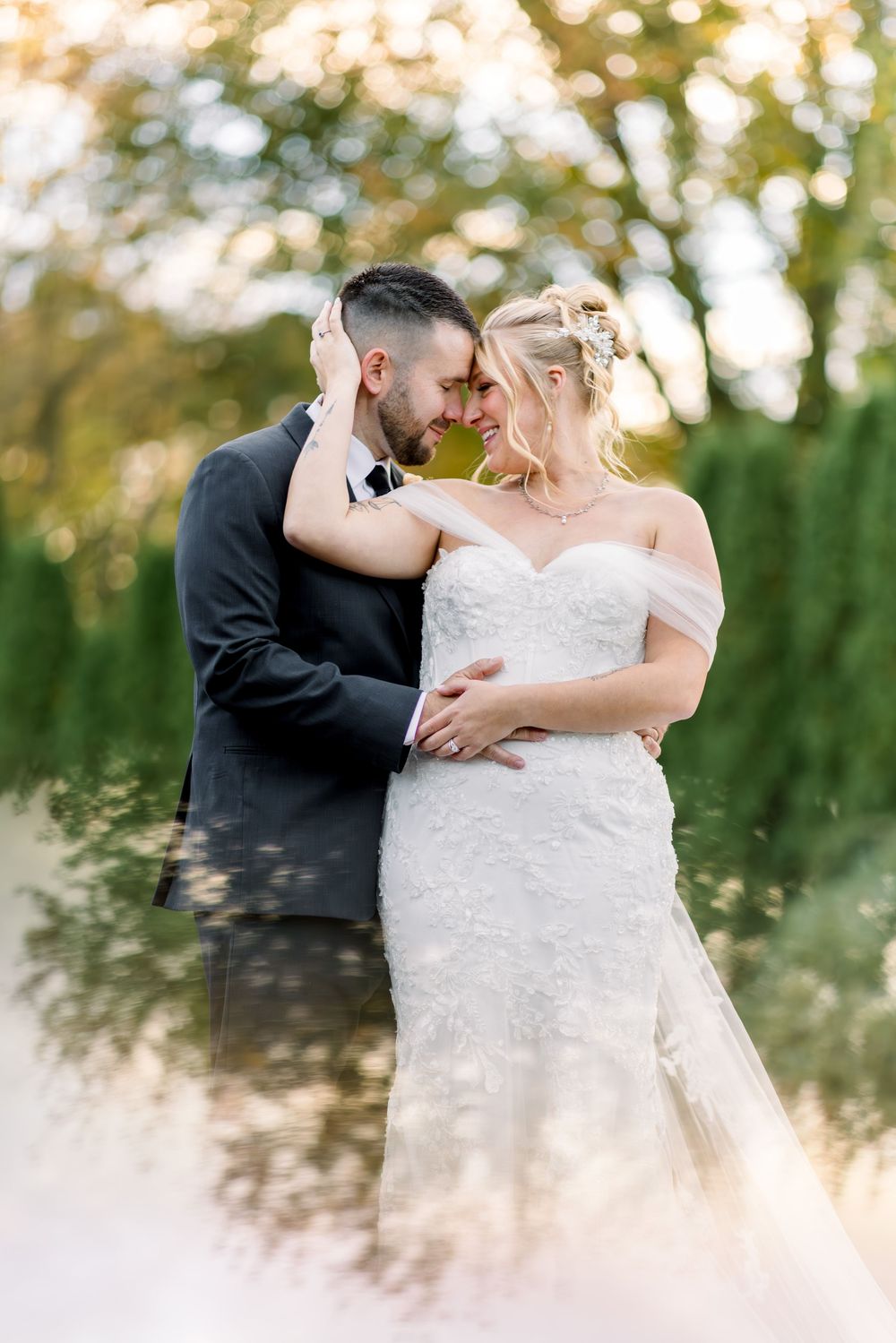 A bride and groom share a romantic forehead touch outdoors, surrounded by lush greenery in golden hour light.